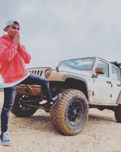 Chad Sig with one foot on the front tire of a mud-covered white Jeep Wrangler on mud-terrain tires
