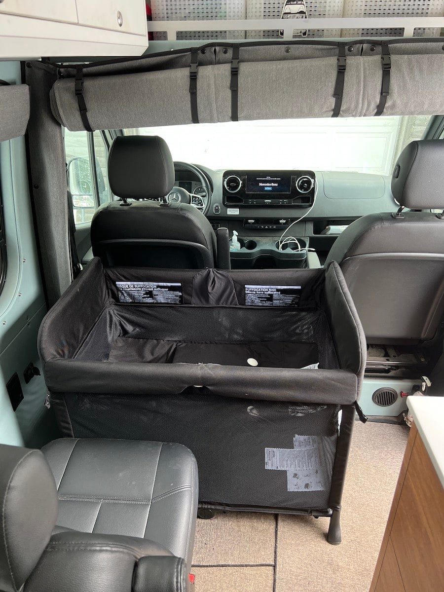 A travel crib wedged into the narrow space between the van's front seats and the rear captain's chair