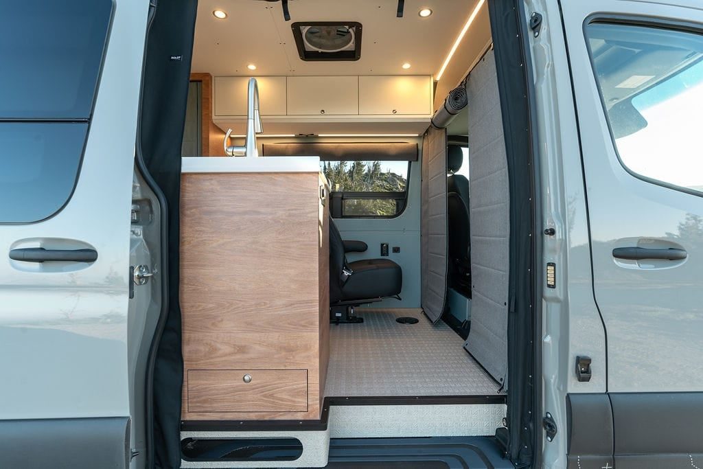 The van's sliding door open, showing a galley cabinet with a sink standing in the doorway and a swivelled seat behind it