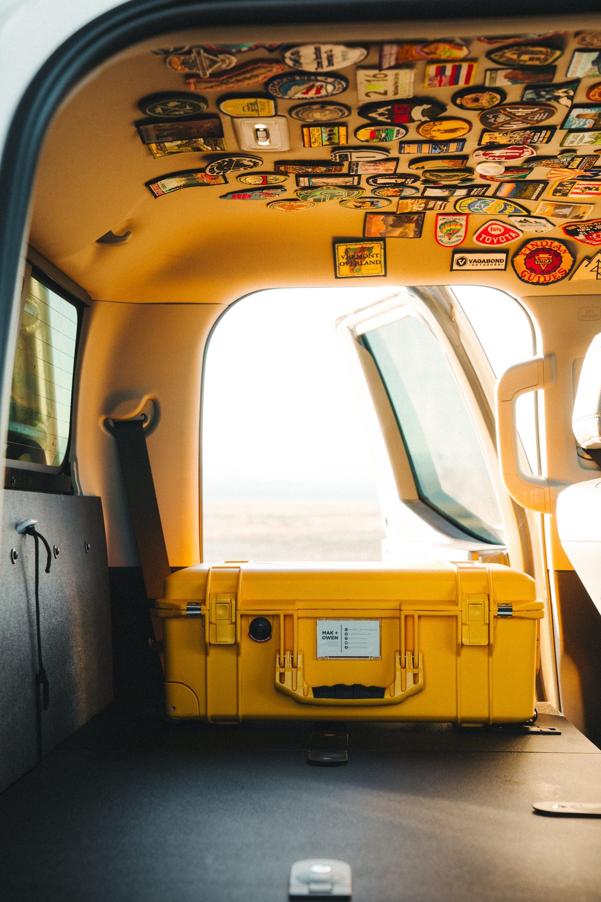 Inside the cab where the rear seats used to be, now a flat deck holding a yellow hard case, with a headliner covered in embroidered patches