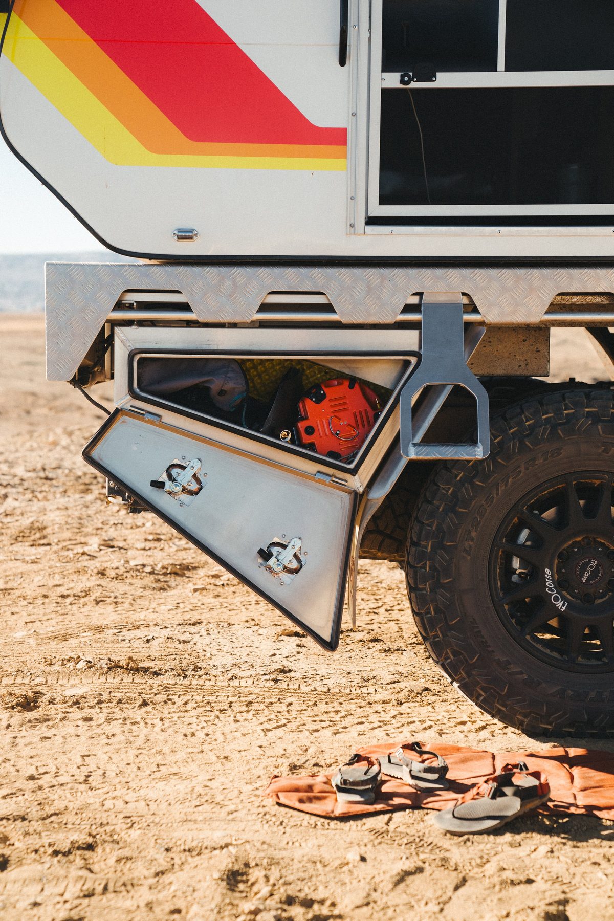 An under-tray toolbox hanging below the tray deck, its drop-down door open on two latches, packed with recovery gear