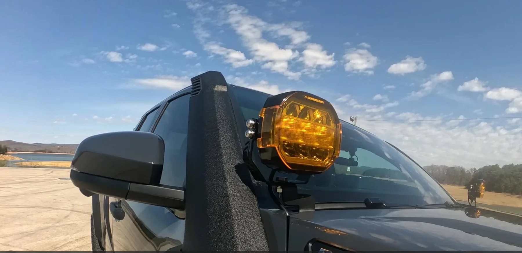 An amber LED pod on a hood-corner bracket beside a snorkel, with its matching pair visible across the hood on the far side