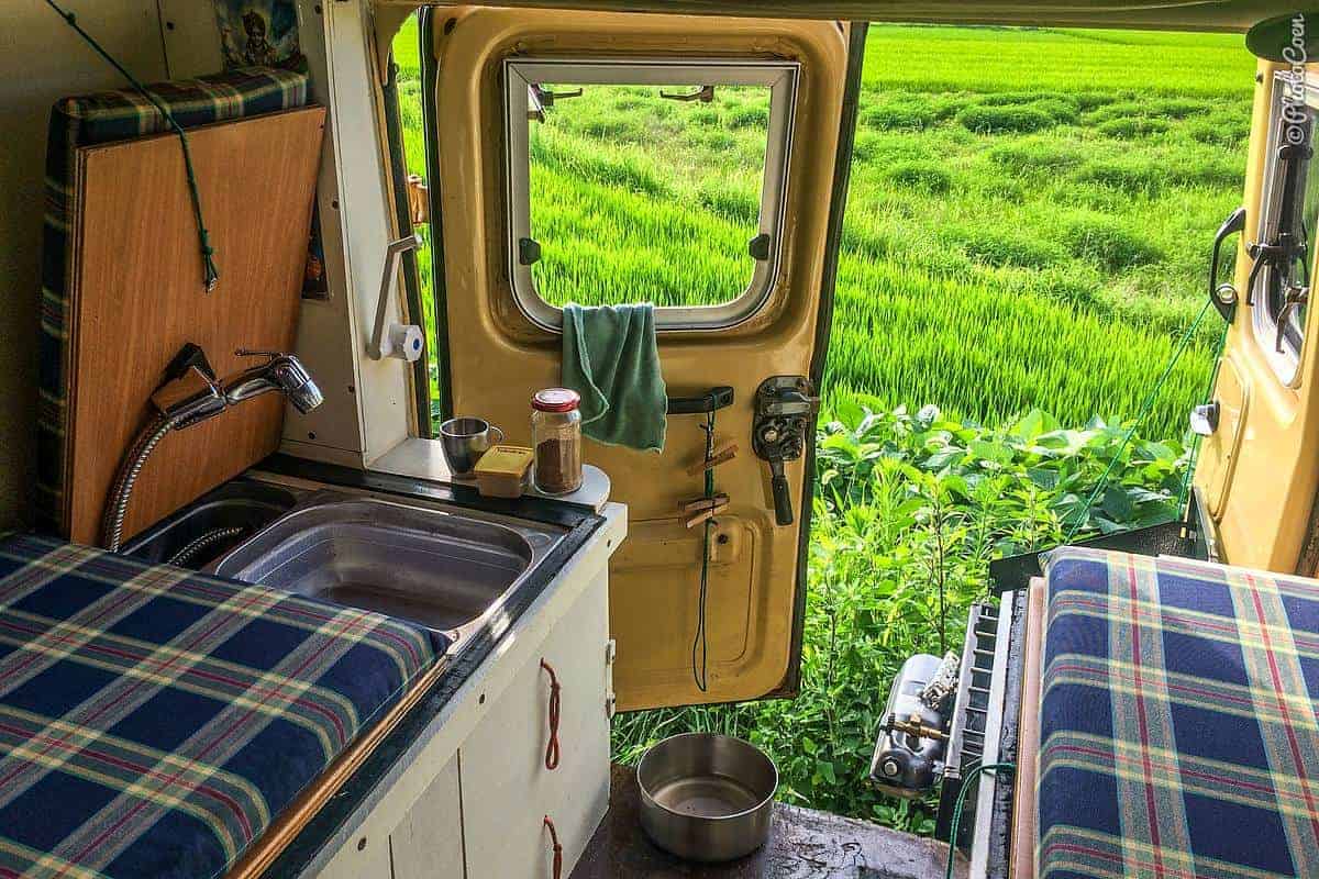 The rear of the Land Cruiser's interior with a small stainless sink and a hand shower on a hose, the rear door open onto a green field