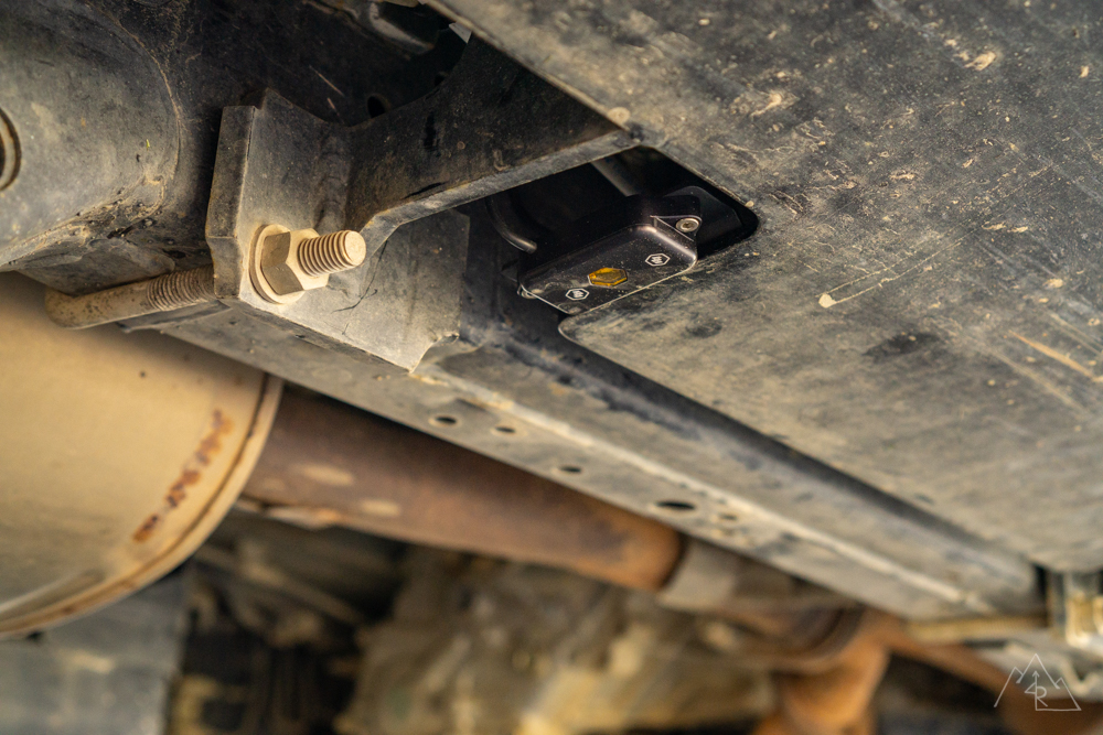 A rock light tucked into a cutout in the underside of a black steel rock slider, with the exhaust pipe running below