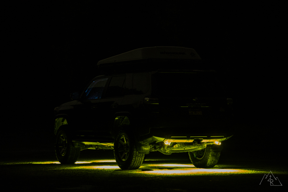 The same 4Runner from the rear quarter at night, amber light pooled along its whole length and behind the rear wheels