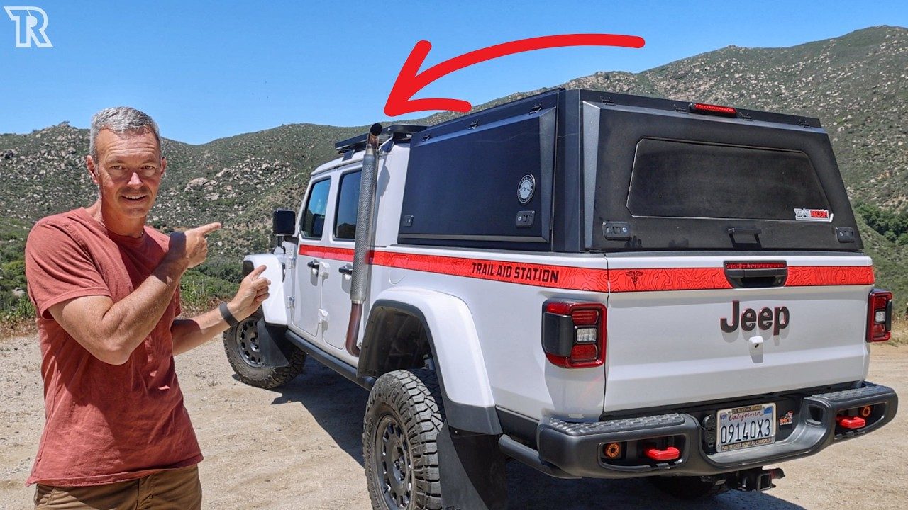 Brad Kowitz standing beside the Gladiator pointing at its raised fording exhaust, with the OVS truck cap and TRAIL AID STATION graphics along the bed