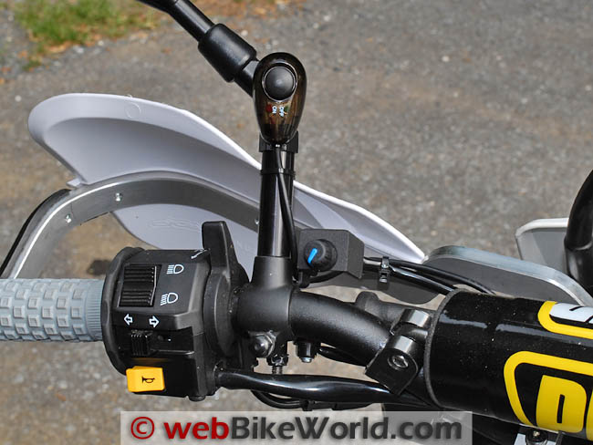The left handlebar of the DR650 with a small round dimmer knob on top of the mirror stalk and a rocker switch on the stalk below it, above the stock switchgear
