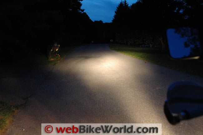 A dark country lane at dusk lit only by the DR650's halogen high beam, a pale oval on the road ahead